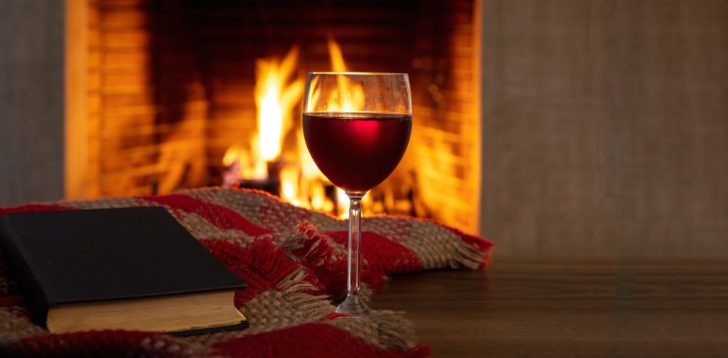 Red wine drinking and reading a book by the fire. Wineglass and a book, burning fireplace background